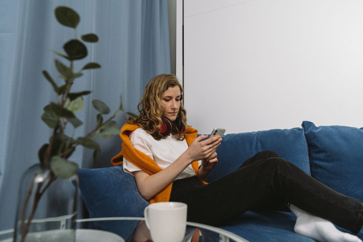 A woman on a blue sofa browsing on her smartphone at home