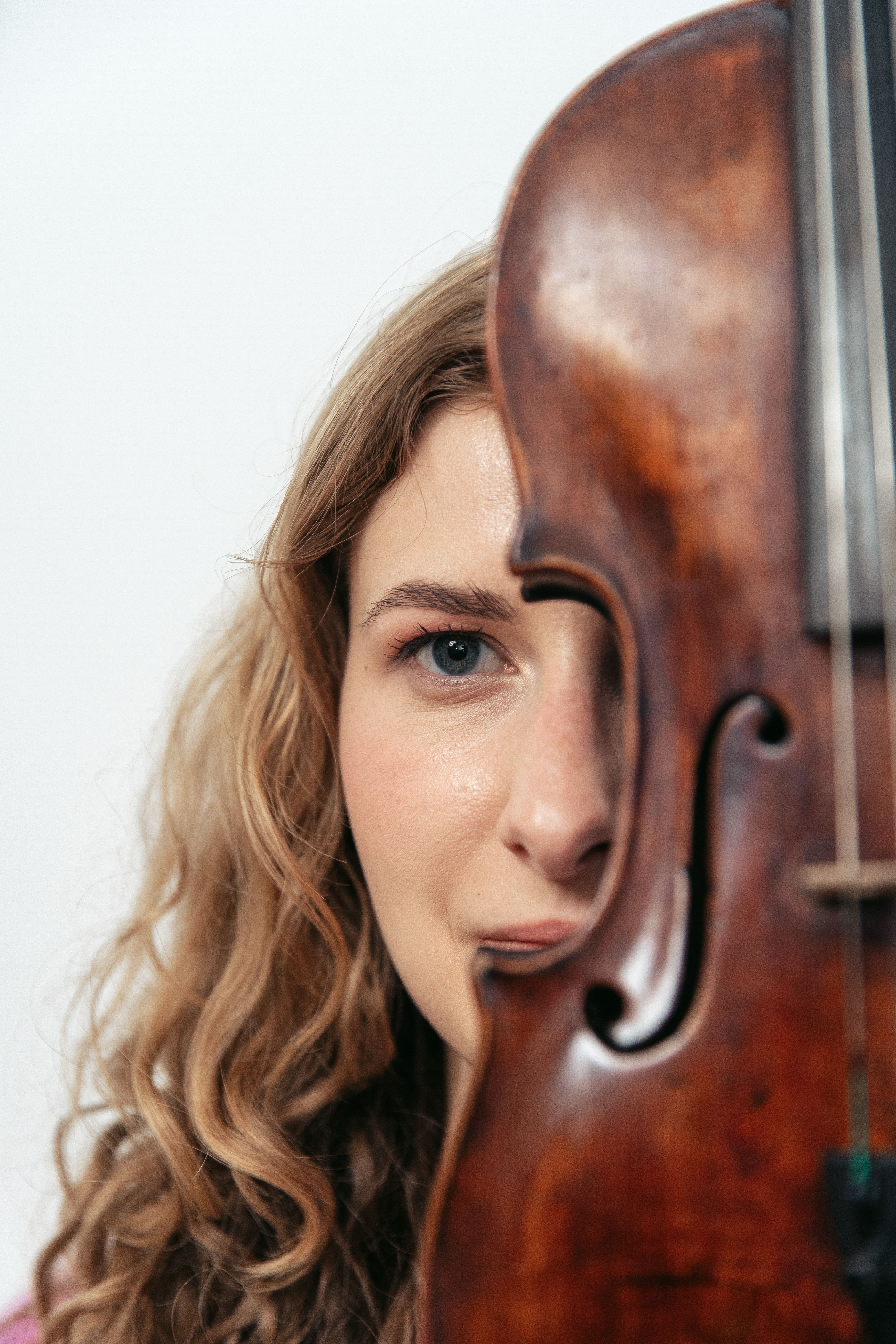 Close-up portrait of a young woman with curly hair, holding a violin.