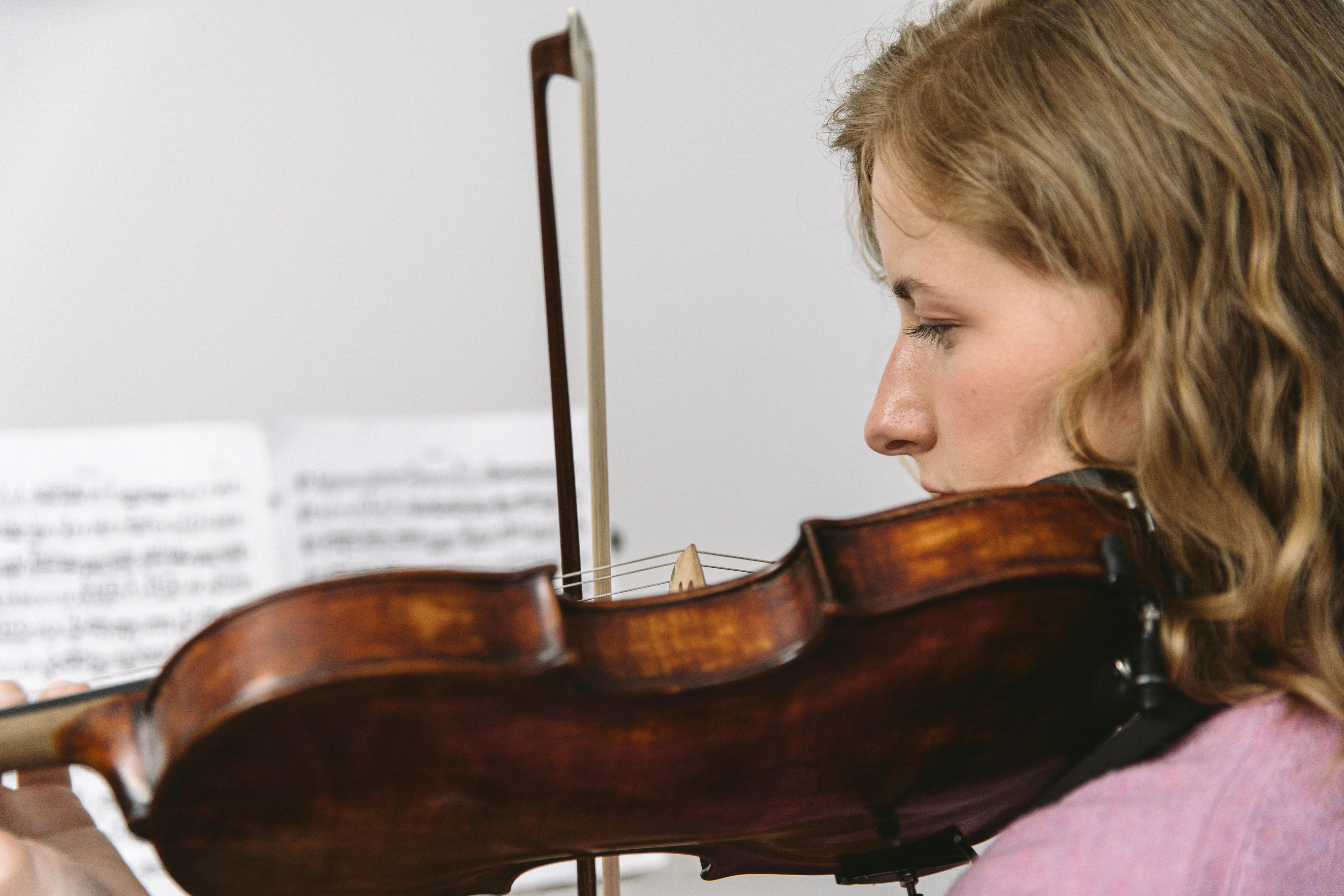 Young woman focused while playing the violin, music sheets visible in the background.