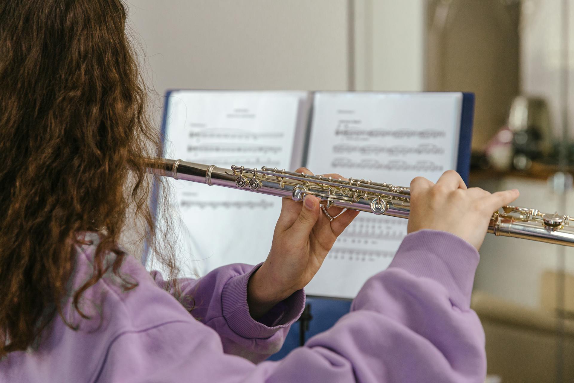 A woman plays the flute while reading sheet music, creating a musical atmosphere.