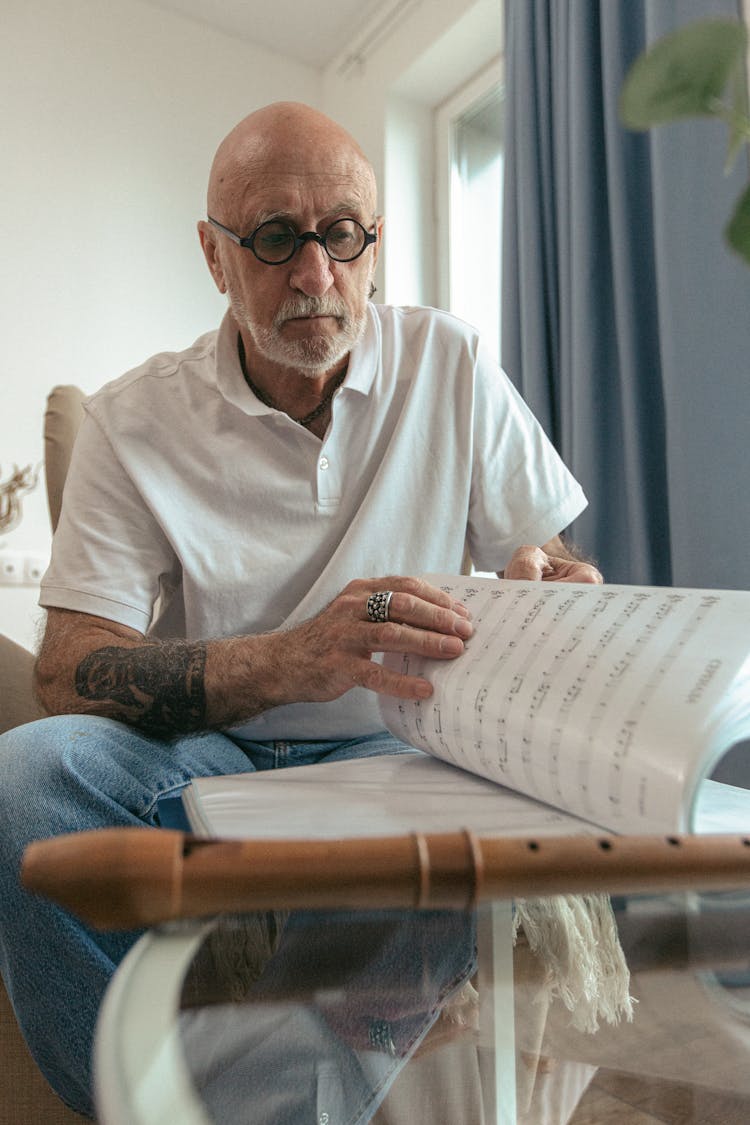 Elderly Man In White Polo Shirt Reading A Music Sheet