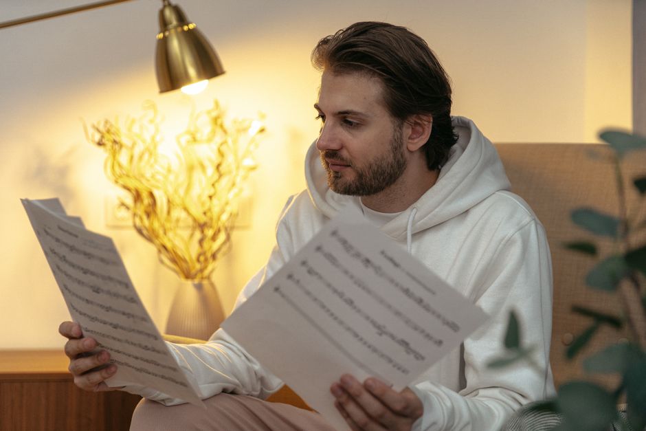 A man sitting in a cozy living room closely reading two pages of sheet music
