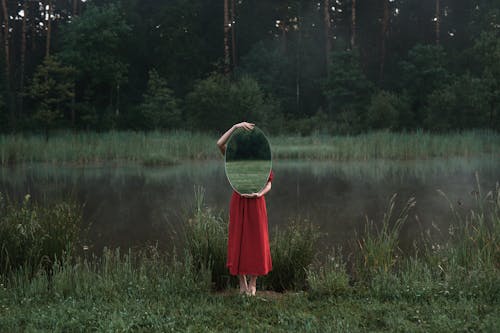 Free A Woman in Red Dress Standing on Green Grass while Holding a Mirror Stock Photo