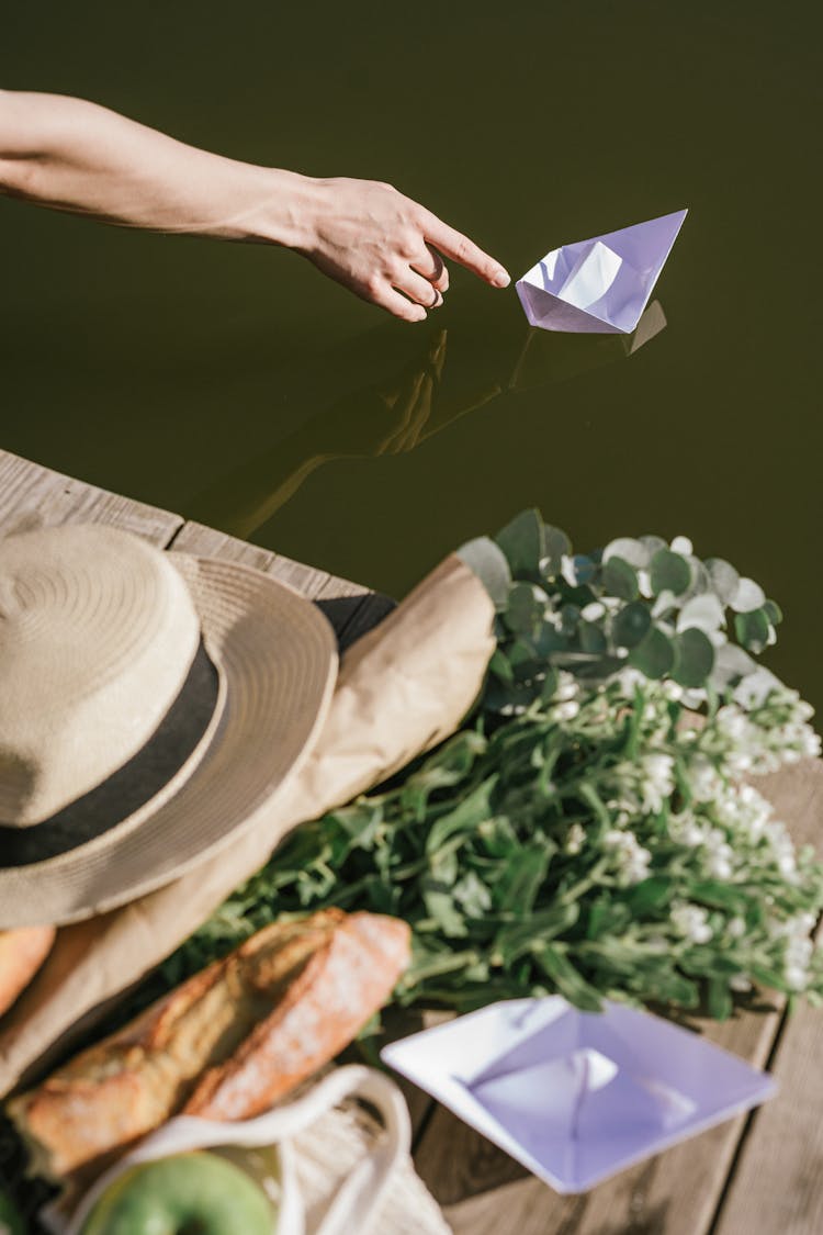 Person Touching A Paper Boat On Water