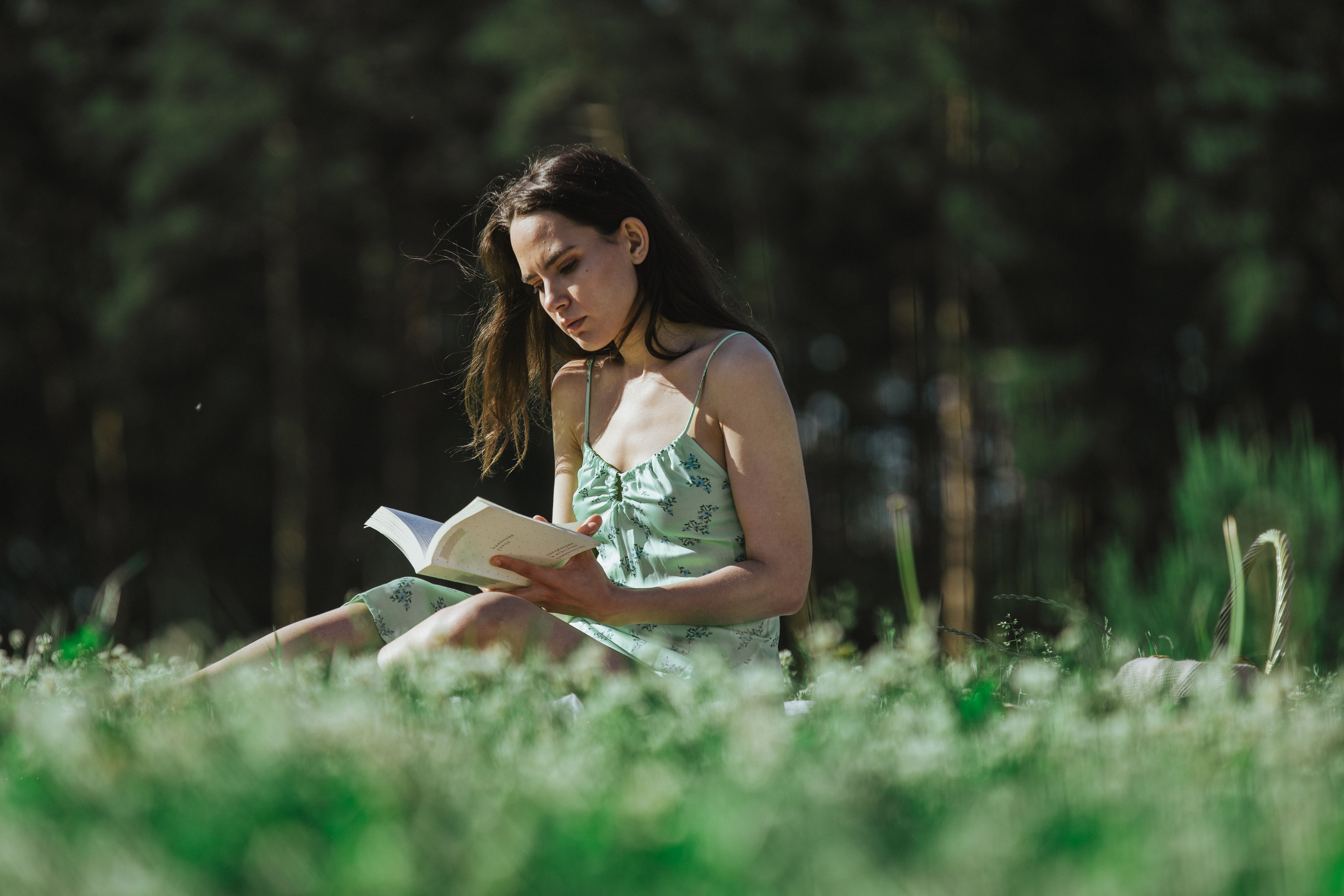 Relaxed young woman enjoys a peaceful reading moment outdoors in a sunny park.
