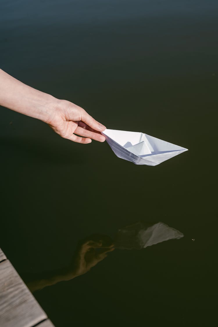 Hand Putting A Paper Boat On The Water