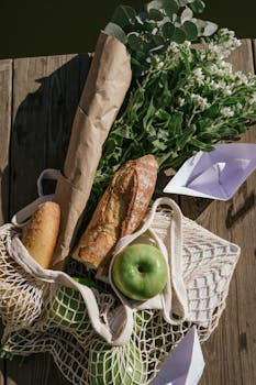 Picnic arrangement featuring fresh bread, green apples, and a flower bouquet on a wooden surface.