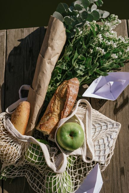 Picnic arrangement featuring fresh bread, green apples, and a flower bouquet on a wooden surface.
