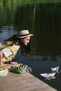 A Woman Sitting on a Wooden Dock while Looking at the Paper Boats Floating on the Lake