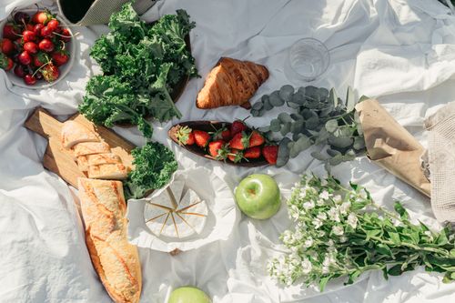 Free Top view of a vibrant picnic spread featuring fresh fruits, breads, and greens on a white cloth. Stock Photo