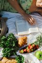 A Woman Lying on a White Blanket Reading a Book