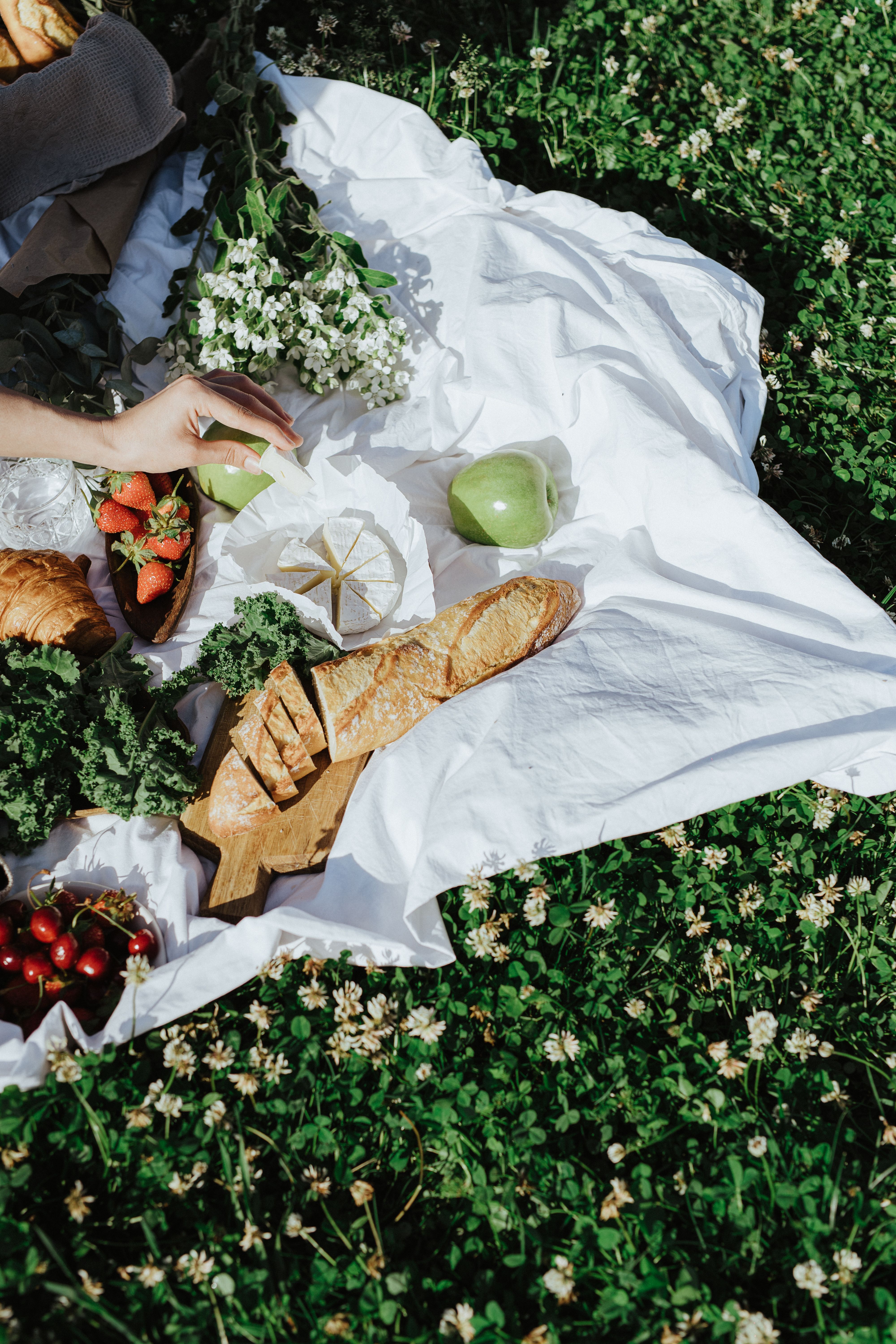 A summer picnic spread with fresh fruits, pastries, and a white blanket on grass.