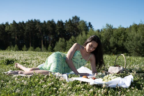 A Woman in Green Dress Lying on a Picnic Blanket while Looking Down