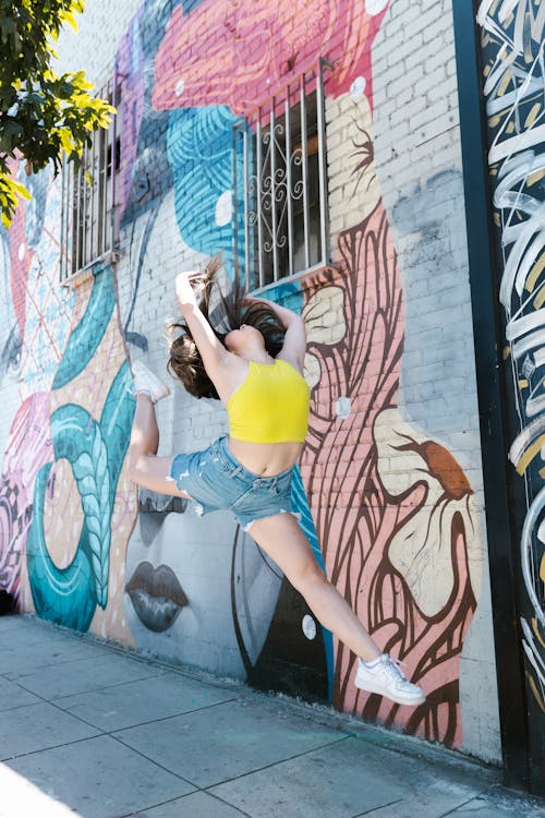 Woman in Yellow Crop Top Jumping near Graffiti Wall