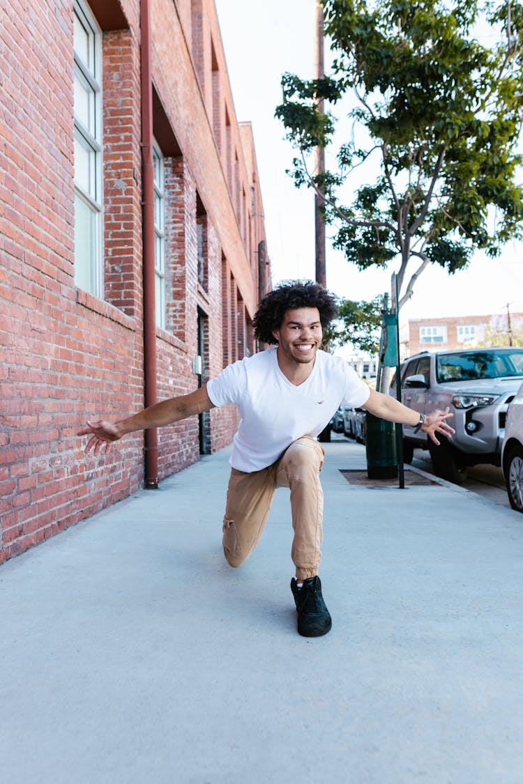 A Man In White Shirt Kneeling On The Side Of The Street Near Brick Building