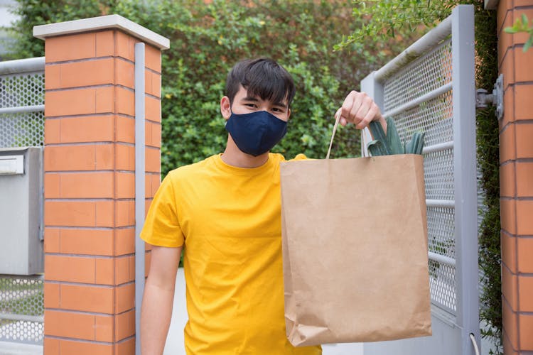 A Man In A Face Mask Holding A Paper Bag Of Groceries