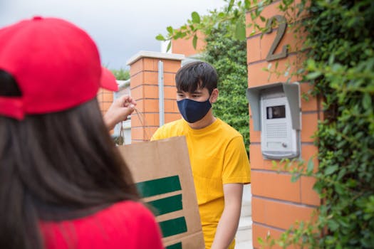 Masked man receiving a delivery from a courier outdoors. Safety measures in place.