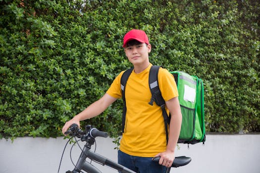 Asian male courier with backpack and bicycle, ready for delivery outdoors.