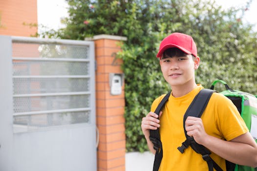 Smiling Asian young man with delivery backpack outside a modern house.