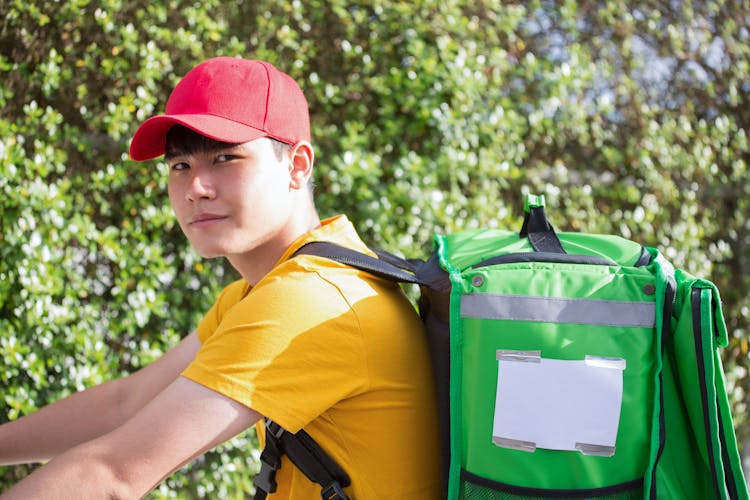 A Man In Red Cap And Yellow Shirt Carrying An Insulated Bag While Looking At The Camera