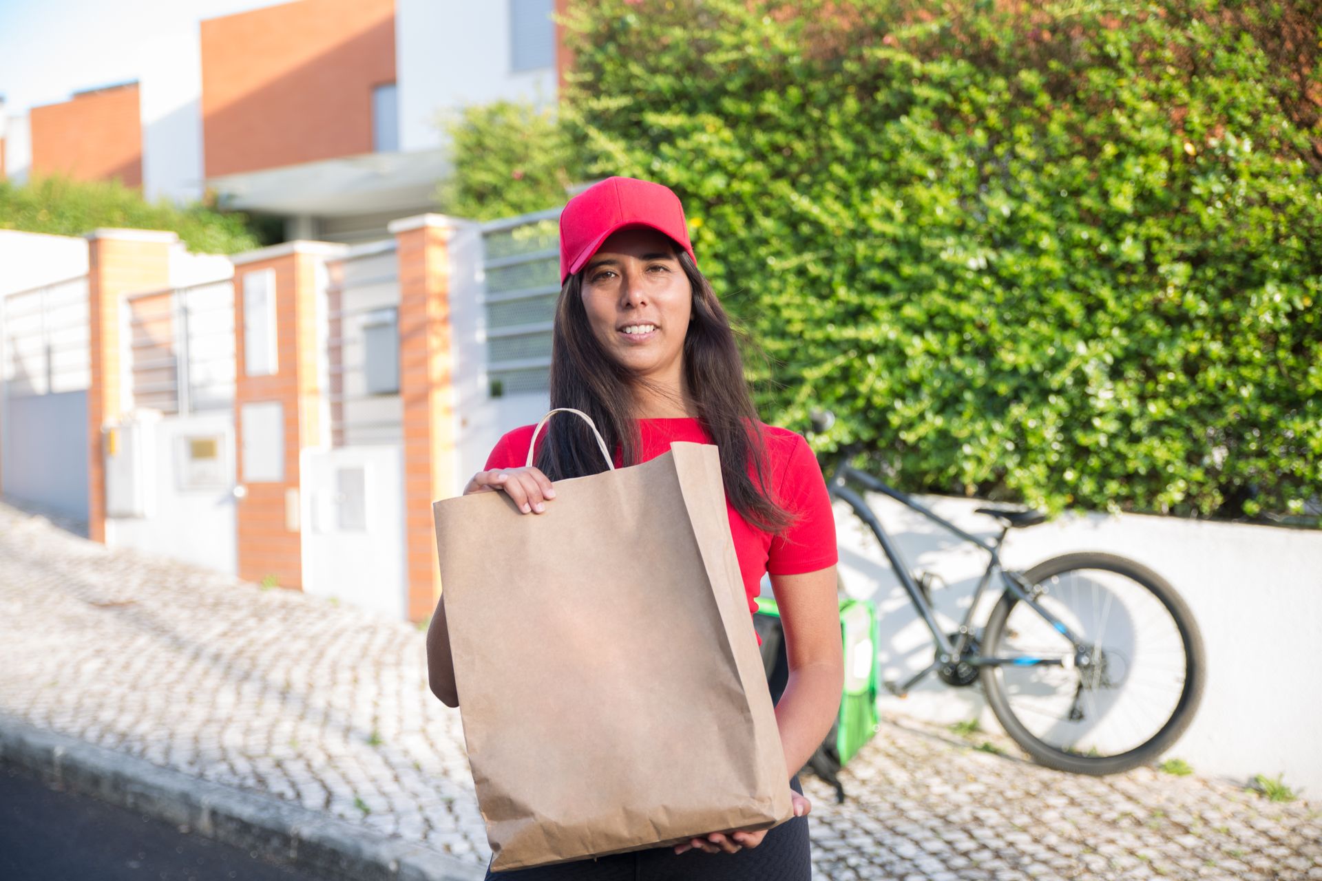 A smiling delivery courier holding a paper grocery bag on a residential street