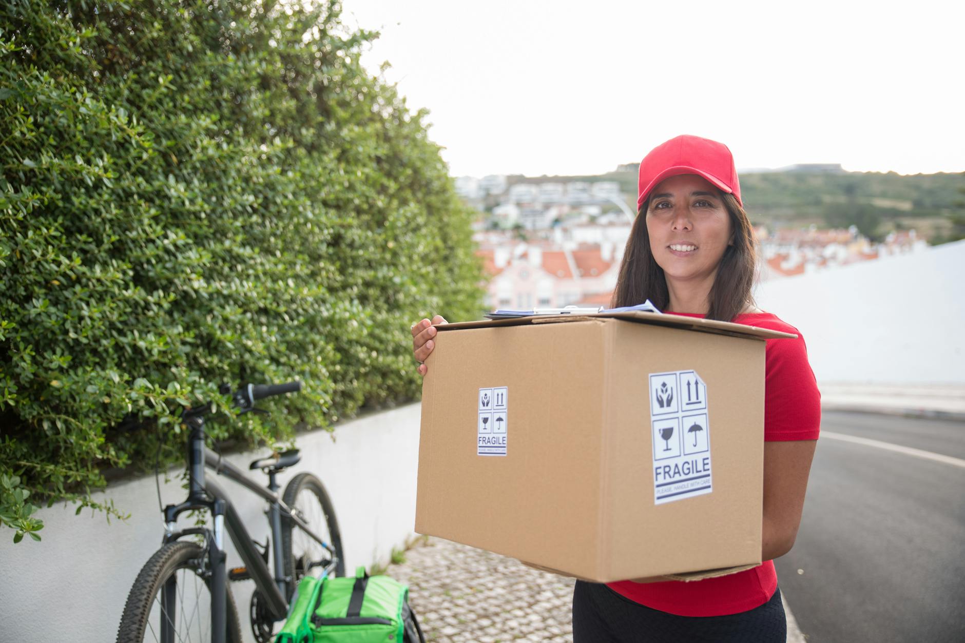 A delivery woman in Portugal carries a package with a bicycle in the background, showcasing urban parcel delivery.