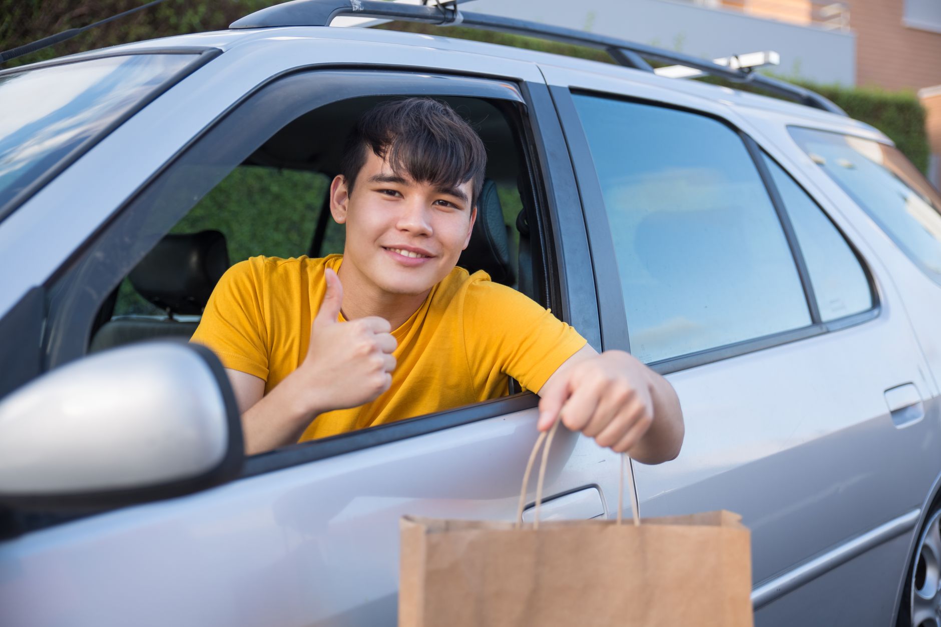 Smiling courier in car delivering a paper bag, offering friendly service.