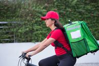 Woman in Red Shirt and Black Pants With Green and Black Backpack Riding Bicycle
