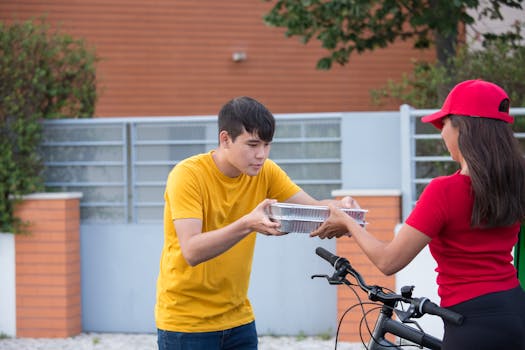 A customer receives a food delivery from a courier on a bicycle outside a home.