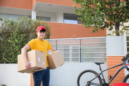 Man Wearing T-shirt and Red Cap Carrying Cardboard Boxes