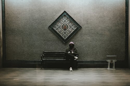 Free A Man in Black Hoodie Sitting on a Metal Bench while Busy Using His Cellphone Stock Photo