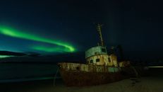 A captivating image of a shipwreck illuminated by the northern lights under a clear night sky.