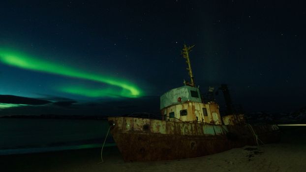 A captivating image of a shipwreck illuminated by the northern lights under a clear night sky.