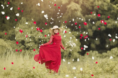 Young Woman in a Red Dress on a Field Among Red and White Flower Petals 