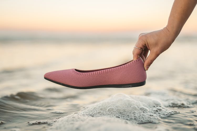 Hand Holding A Pink Flat Shoe Near The Seashore 