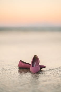 Elegant pink shoes on a calm beach during sunset, epitomizing style and simplicity.