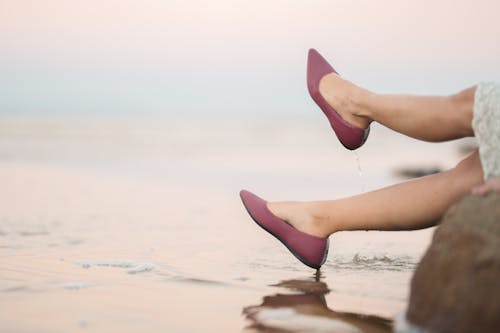 Person Wearing Maroon Flat Shoes on Water