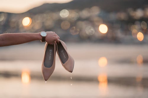 A Person Holding a Wet Brown Slip on Shoes