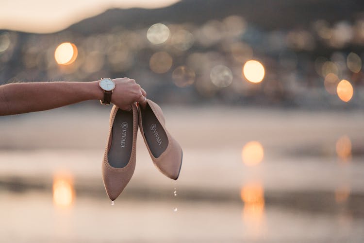 A Person Holding A Wet Brown Slip On Shoes