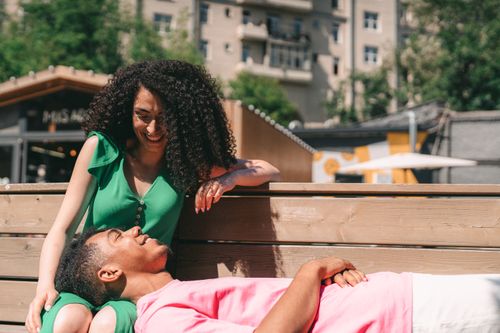 Free A happy couple enjoys a sunny day on a bench, showcasing love and leisure in an urban setting. Stock Photo