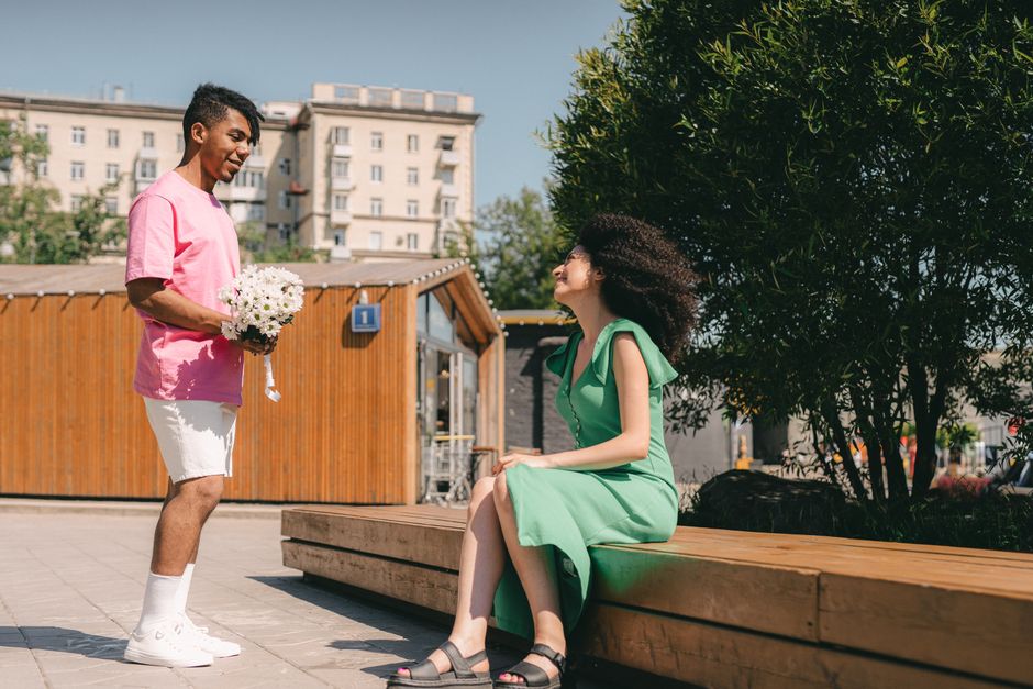 Man surprises woman with flowers in a romantic outdoor setting.