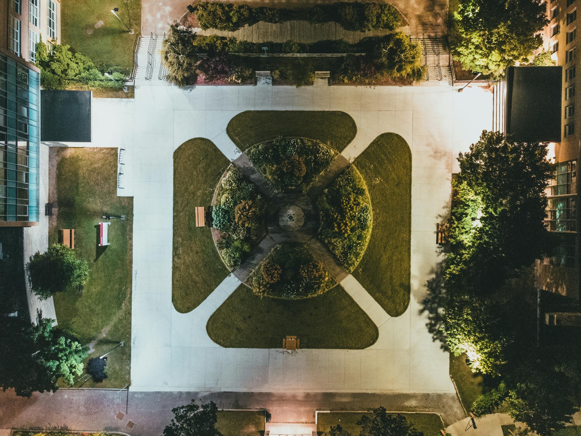 A mesmerizing aerial view of a symmetrical urban park, illuminated at night, showcasing pathways and greenery.