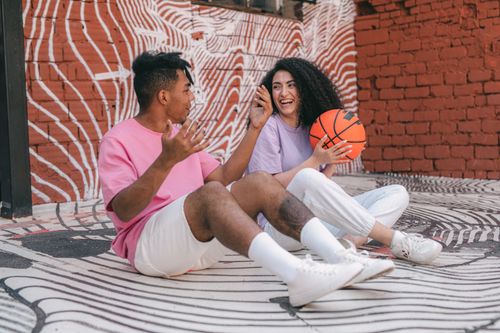 Free Happy couple sitting against colorful graffiti wall, holding basketball. Stock Photo