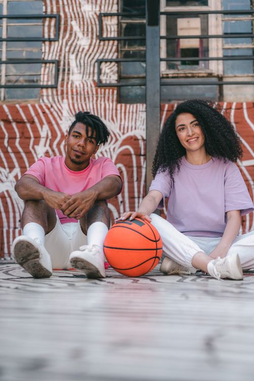 Free Happy couple sitting on the floor with a basketball, set against a graffiti art background. Stock Photo