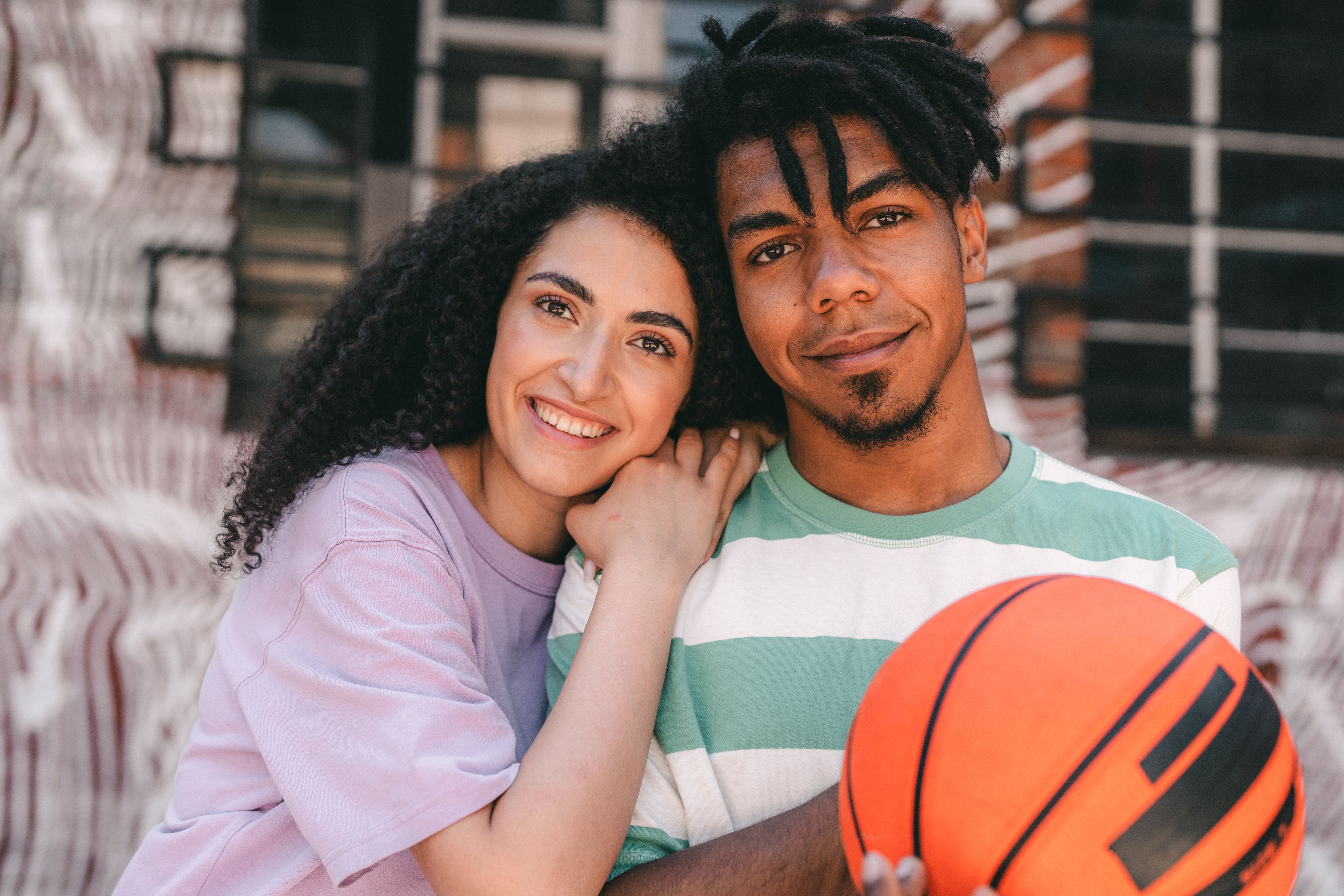 Interracial couple with a basketball, smiling and embracing outdoors.