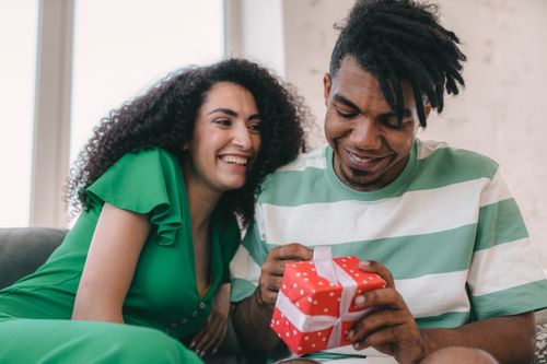 Free A happy interracial couple enjoys a gift exchange at home, capturing a moment of joy and connection. Stock Photo