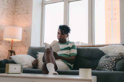 Young man reading a book in a cozy living room with natural light.
