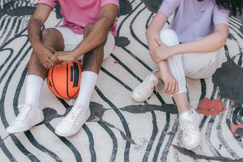 Free Two friends sitting on patterned pavement with a basketball, enjoying a casual outdoor moment. Stock Photo