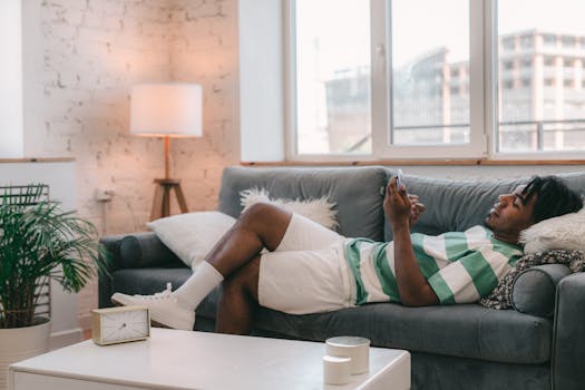 African American man relaxing on a sofa while using a smartphone in a cozy living room setting.
