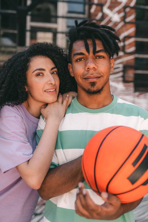 Free Happy interracial couple embracing while man holds a basketball outdoors, smiling and enjoying the day. Stock Photo